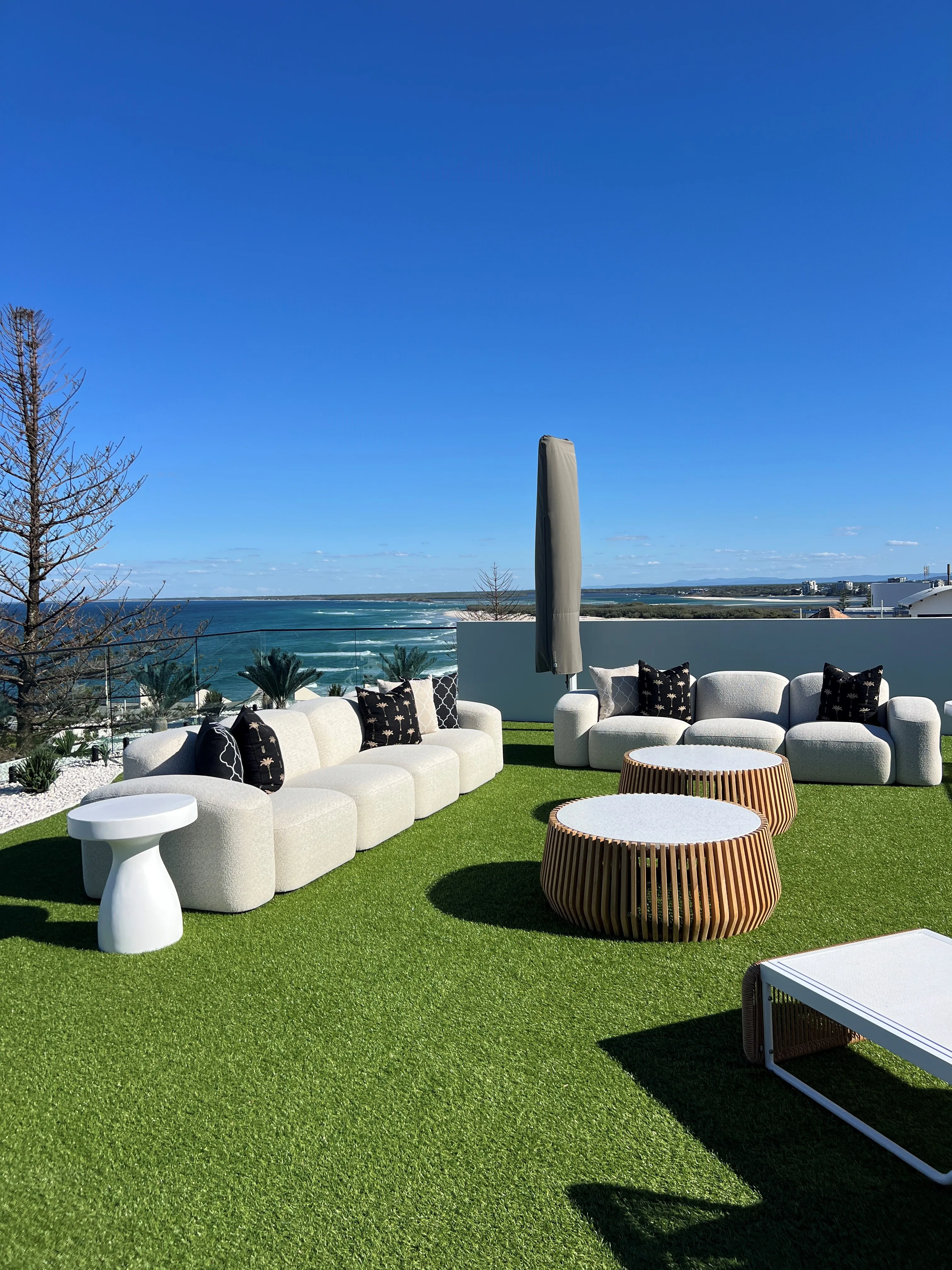 Rooftop terrace lounge with white bouclé modular sofa, slatted coffee table and panoramic ocean backdrop